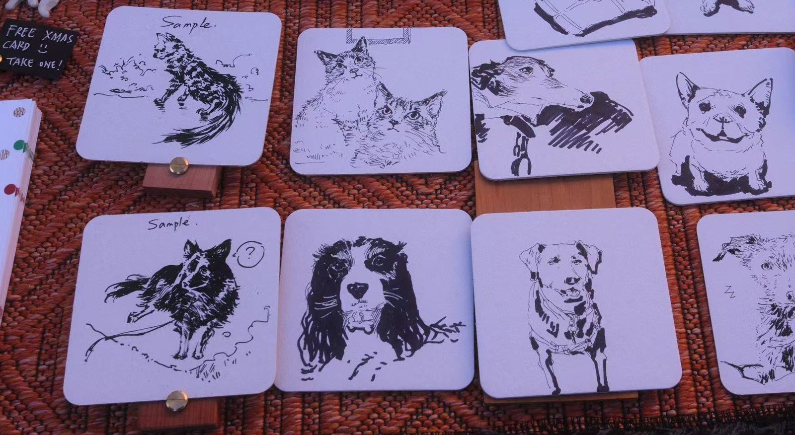 Ink drawings of cats and dogs on white coasters laid out on a woven rug