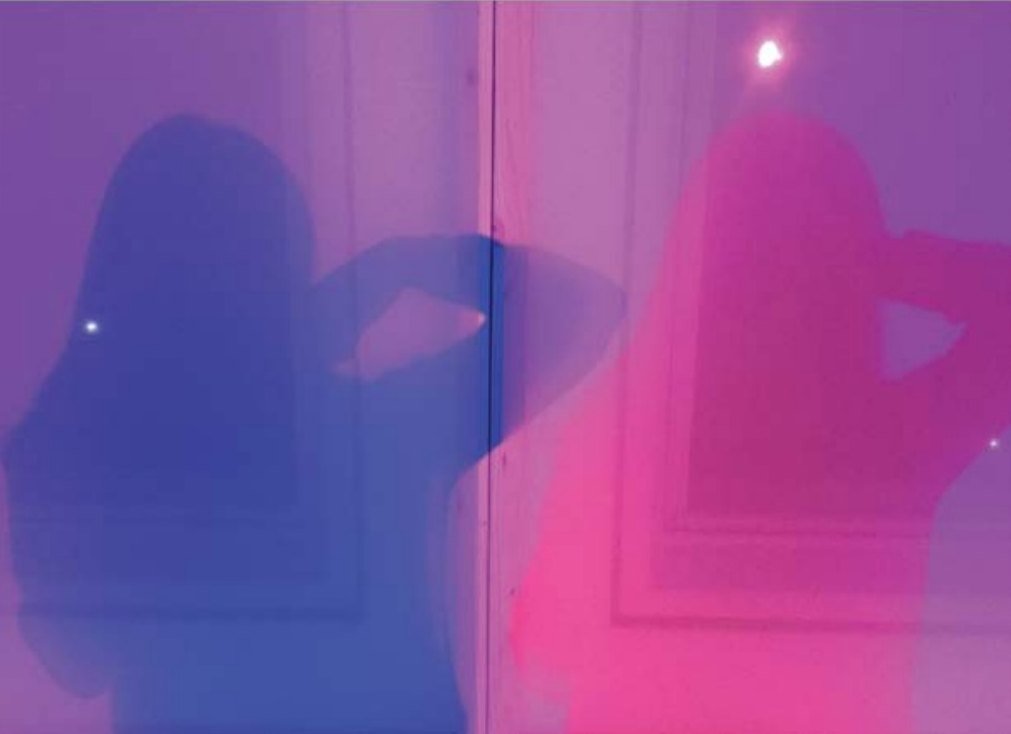 Blue and magenta shadows of two people cast on a lit window screen