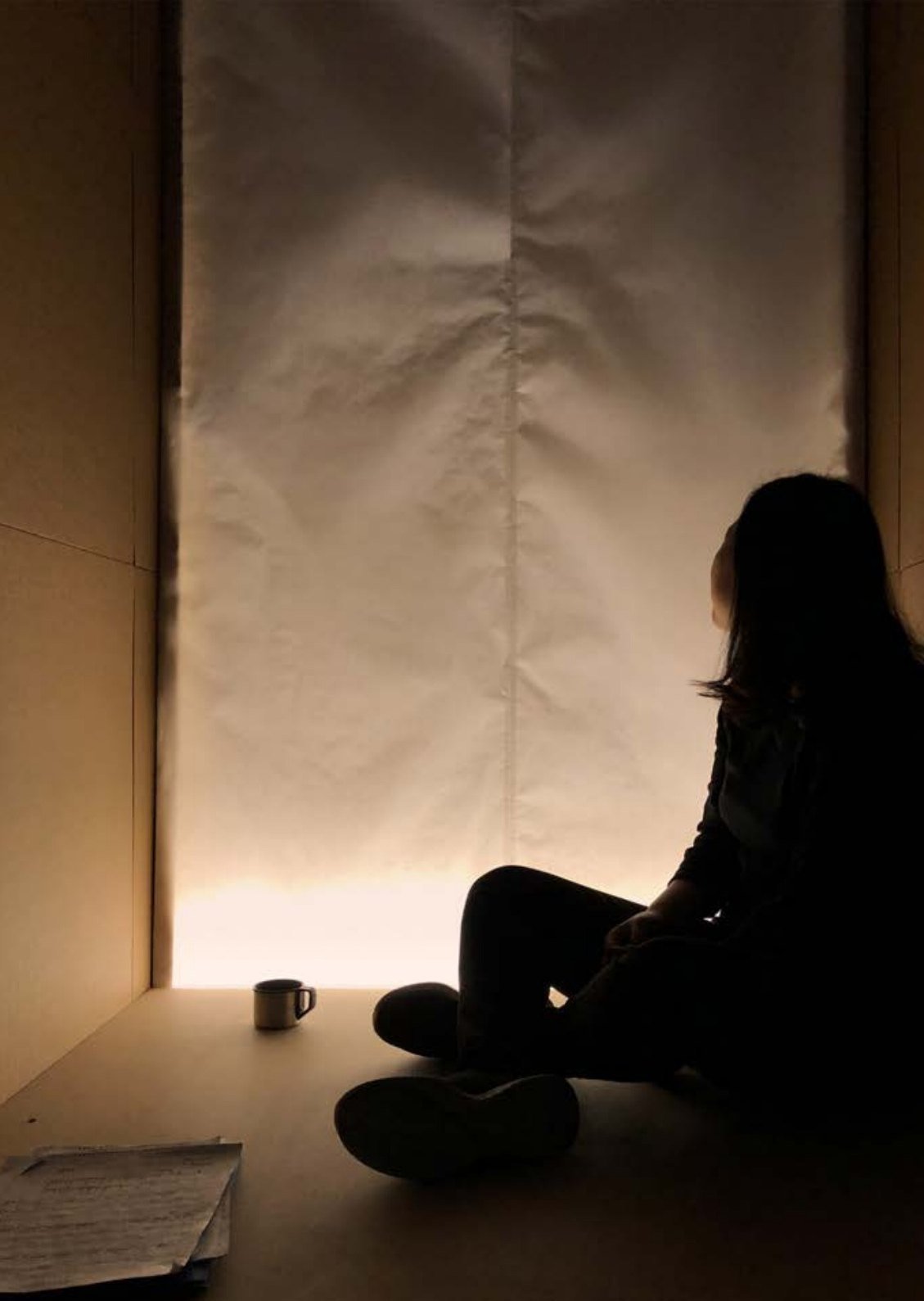 Silhouette of a person seated before a glowing rice-paper wall