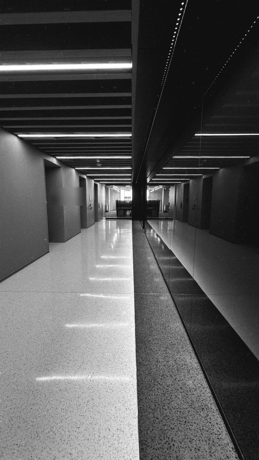Elevator lobby with linear slot lights between ceiling baffles reflected in a polished terrazzo floor