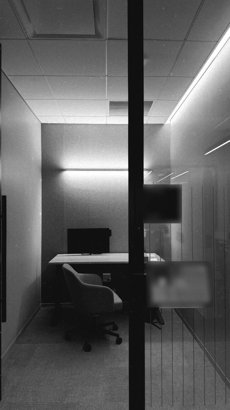 Small glass-walled focus room with a desk lit by a linear wall grazer