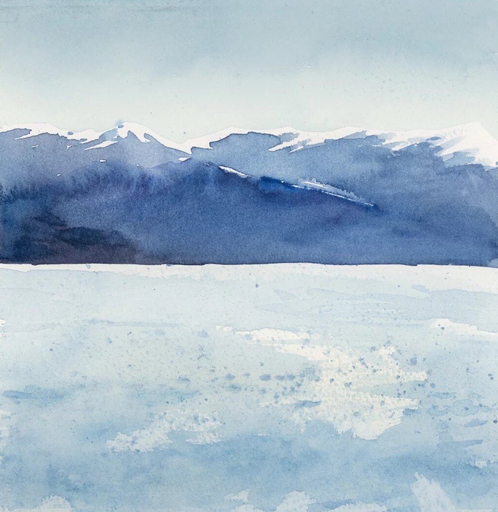 Snow-capped blue mountains above a pale, sparkling lake